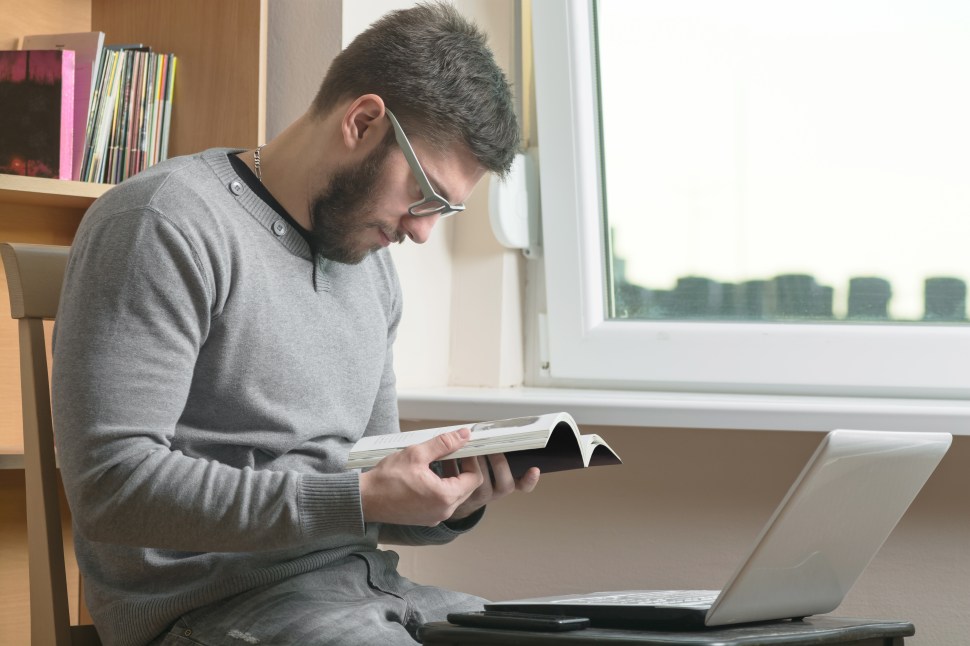 Young adult man reading book at office